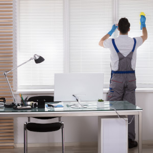 Eine Reinigungskraft reinigt bei der Fensterreinigung auch die Jalousien
