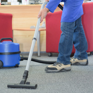 Eine Reinigungskraft saugt den Teppich eines Büros ab