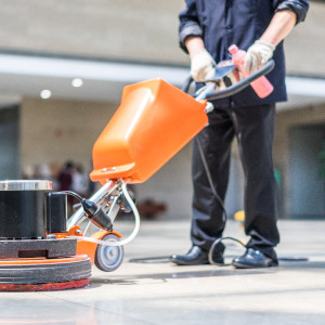 Ein Mitarbeiter der Gebäudereinigung führt die maschinelle Grundreinigung von Boden aus